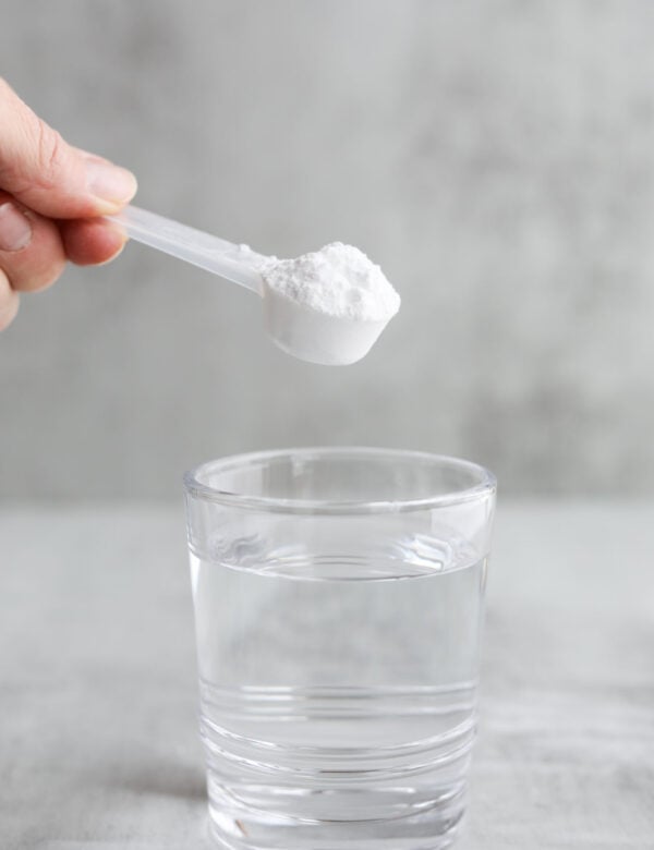 A small scooper filled with white powder creatine being held over a glass of water