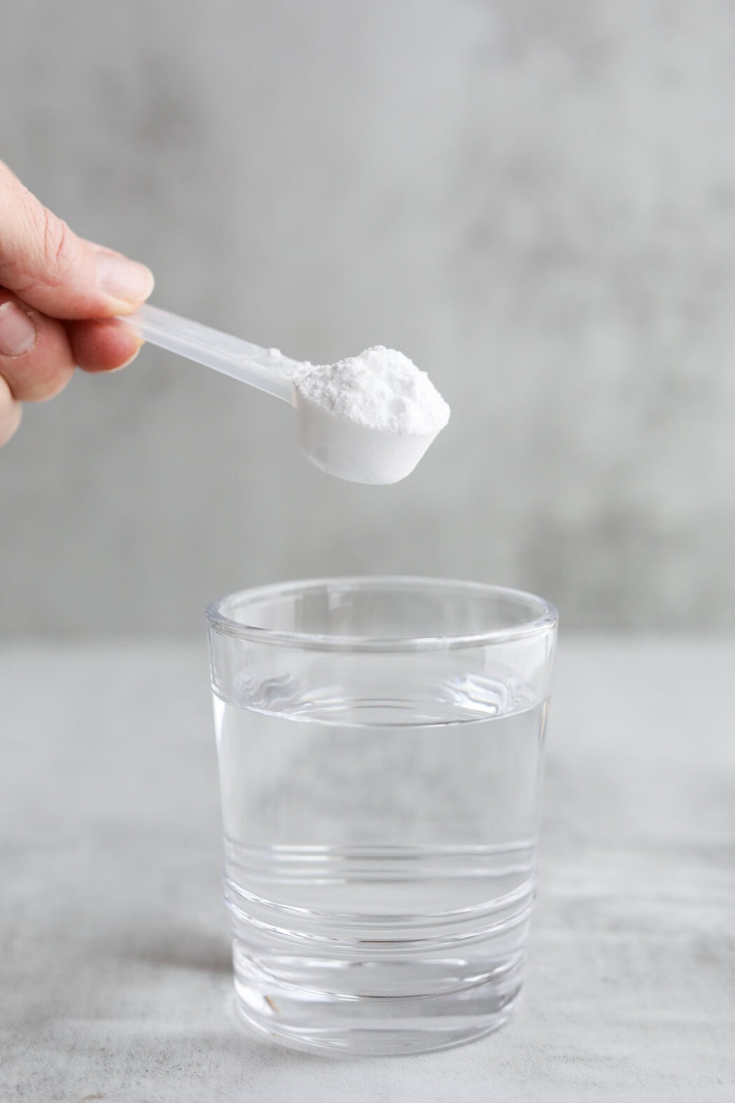 A hand holding a scoop of Creatine powder over a glass of water. 