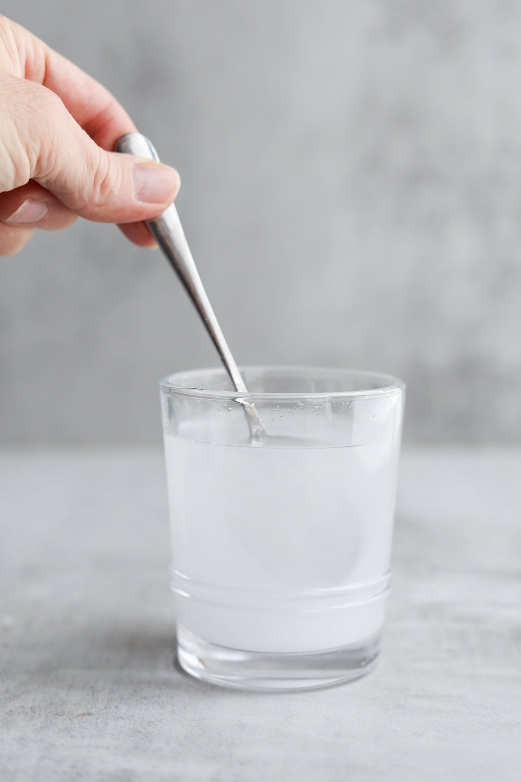 A hand holding a spoon stirring Creatine powder into a glass of water. 