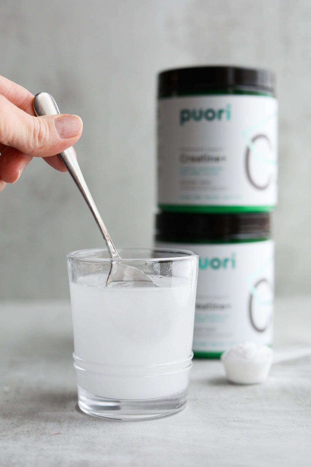 Close up view of a hand holding a spoon stirring creatine powder in a glass of water. 