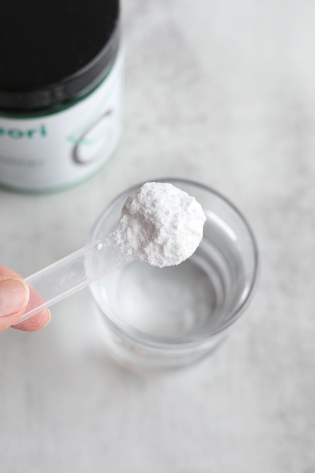 Overhead view of a scoop filled with Creatine powder above a glass of water. 