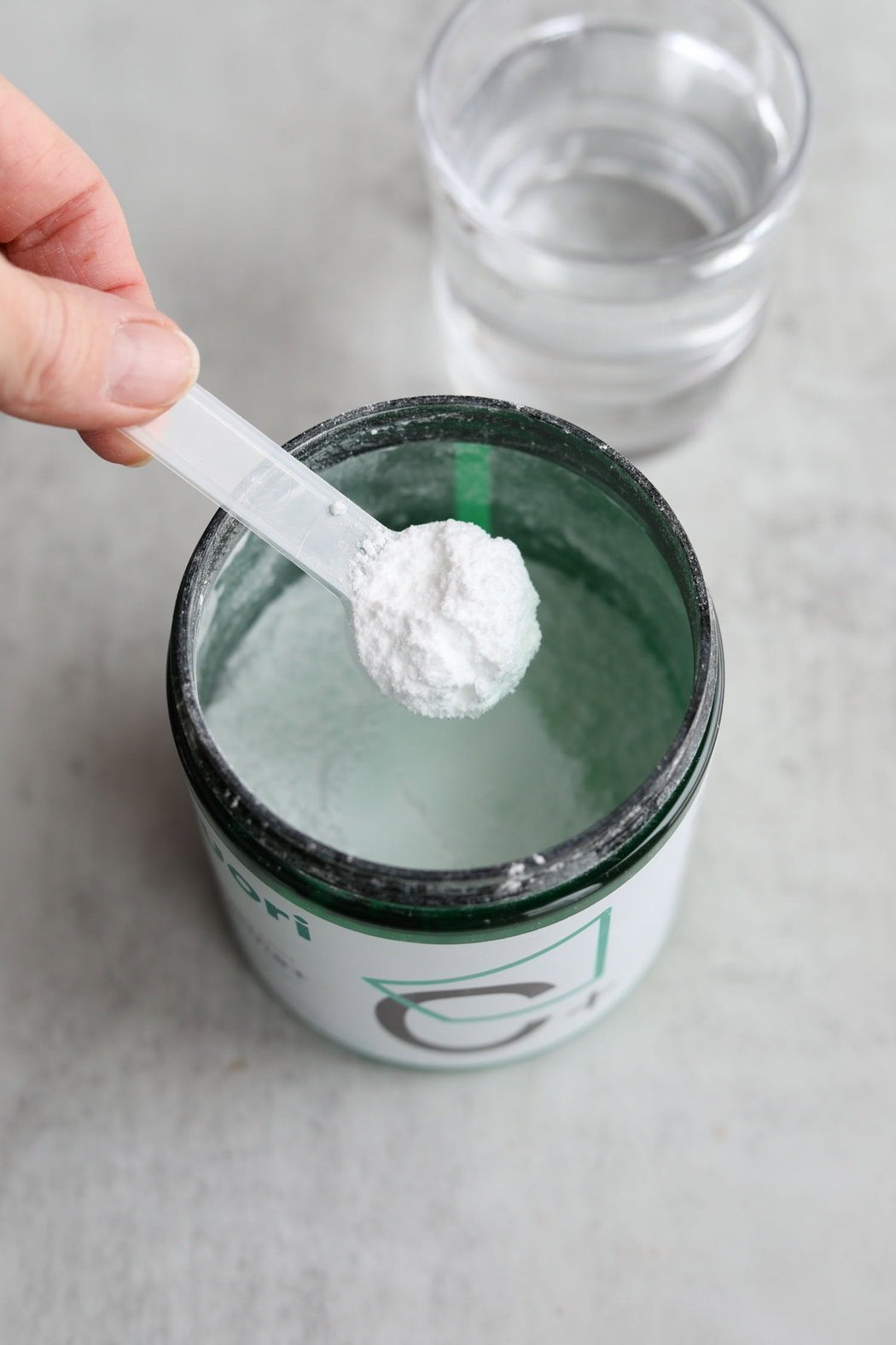 Overhead view of a hand holding a scoop filled with creatine powder above the canister. 