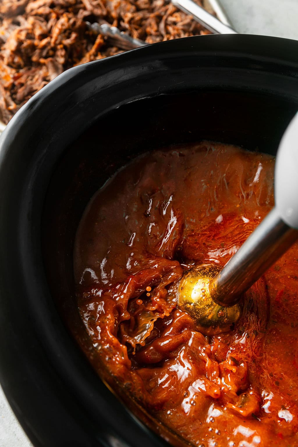 Overhead view of Crockpot Birria Tacos mixture in a slow cooker being mixed with an emersion blender. 