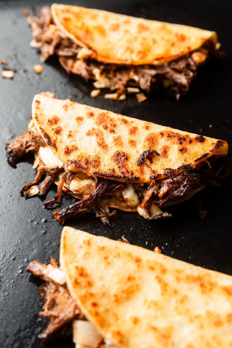 Overhead view of a skillet with birria tacos warming on top crisping the edges of the tortilla shells.
