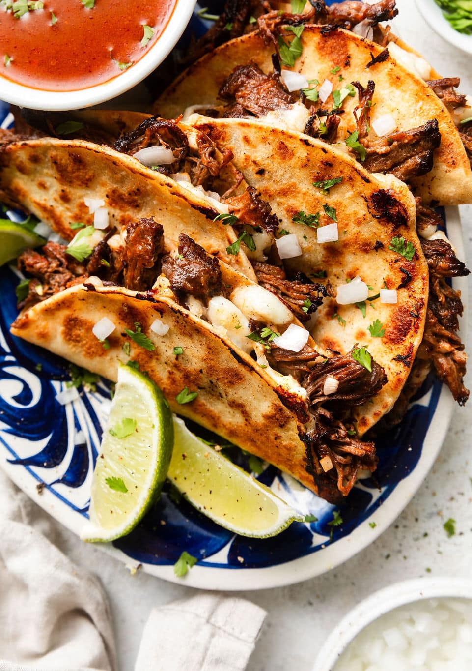 Close up view of a plate of Crockpot Birria Tacos (Quesabirria) topped with fresh cilantro and white onion. 