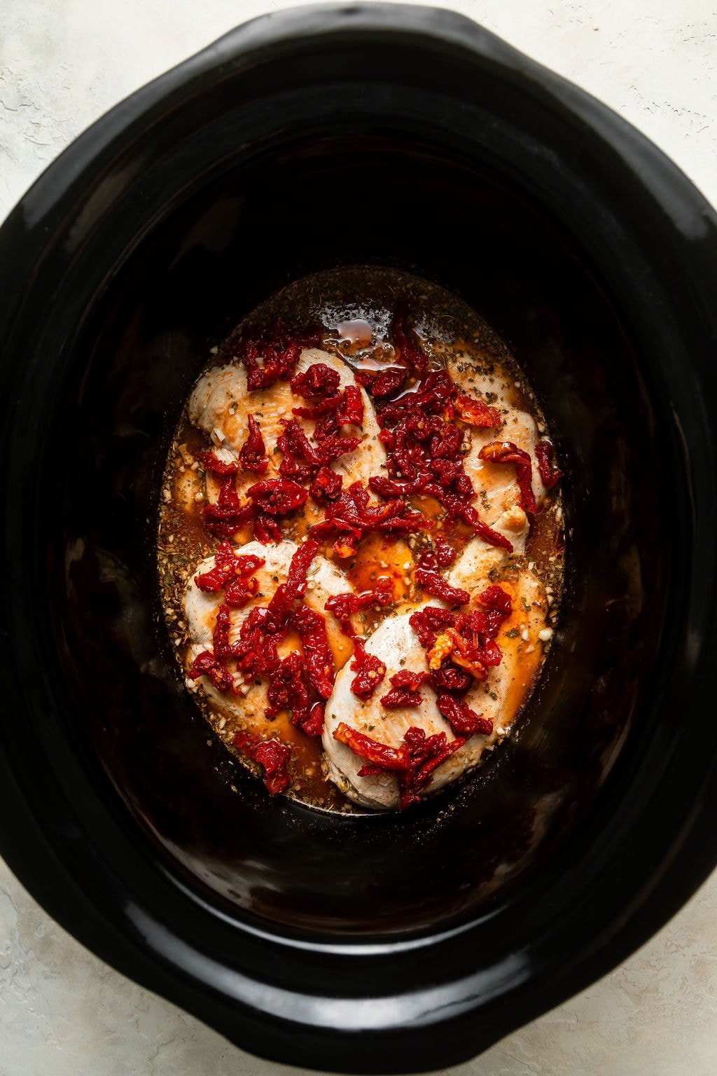 Overhead view of a slow cooker filled with Crockpot Marry Me Chicken ingredients. 