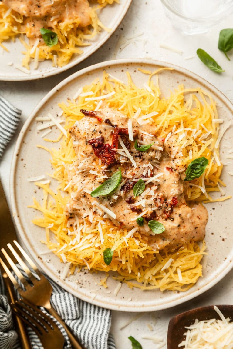 Overhead view of a plate of spaghetti squash topped with marry me chicken and fresh basil. 