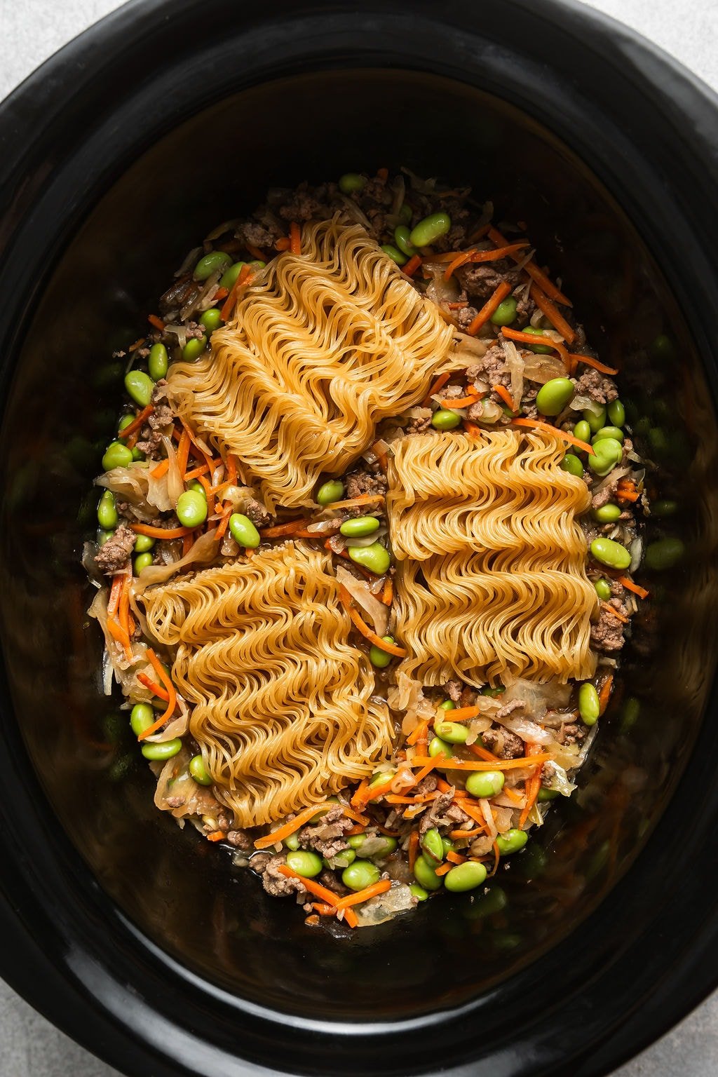 Overhead view of a crockpot filled with Crockpot Beef Ramen ingredients ready for cooking. 