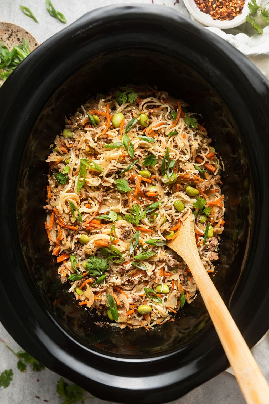 Overhead view of a crockpot filled with Crockpot Beef Ramen topped with green onions and cilantro. 