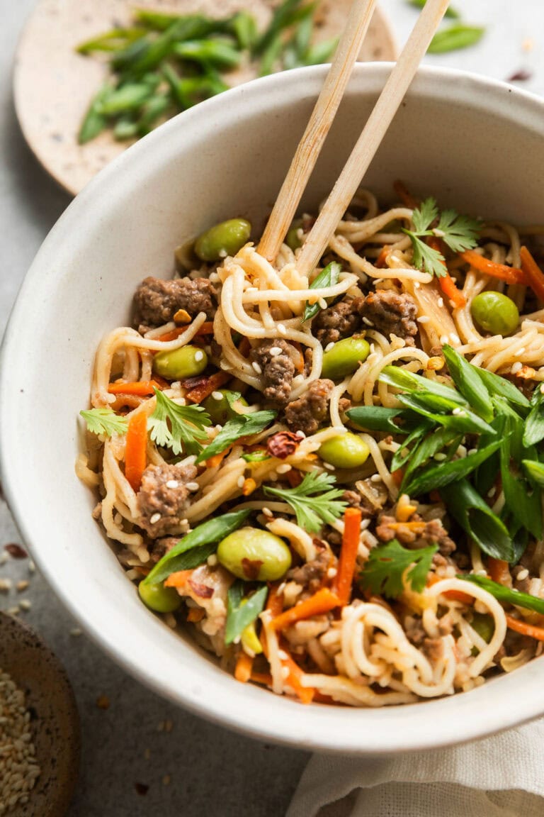 Close up view of a bowl of crockpot beef ramen topped with edamame beans and sesame seeds. 
