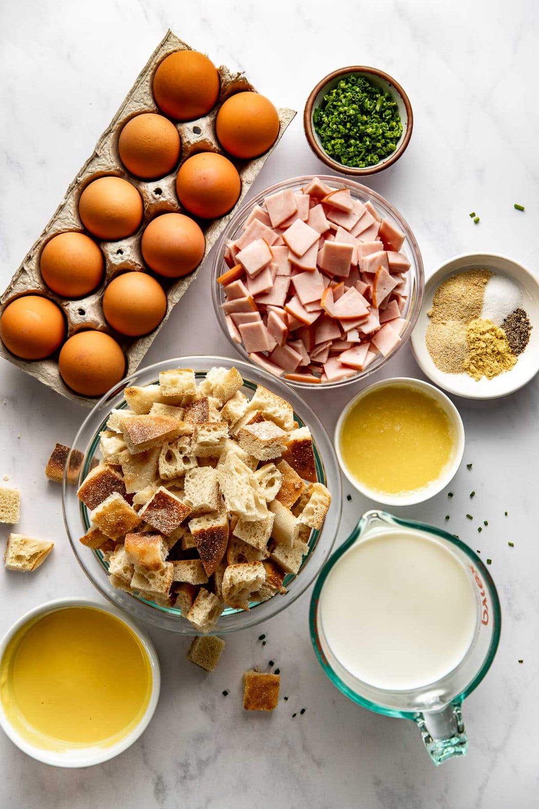 Overhead view of a variety of ingredients for Eggs Benedict Casserole in different sized bowls. 