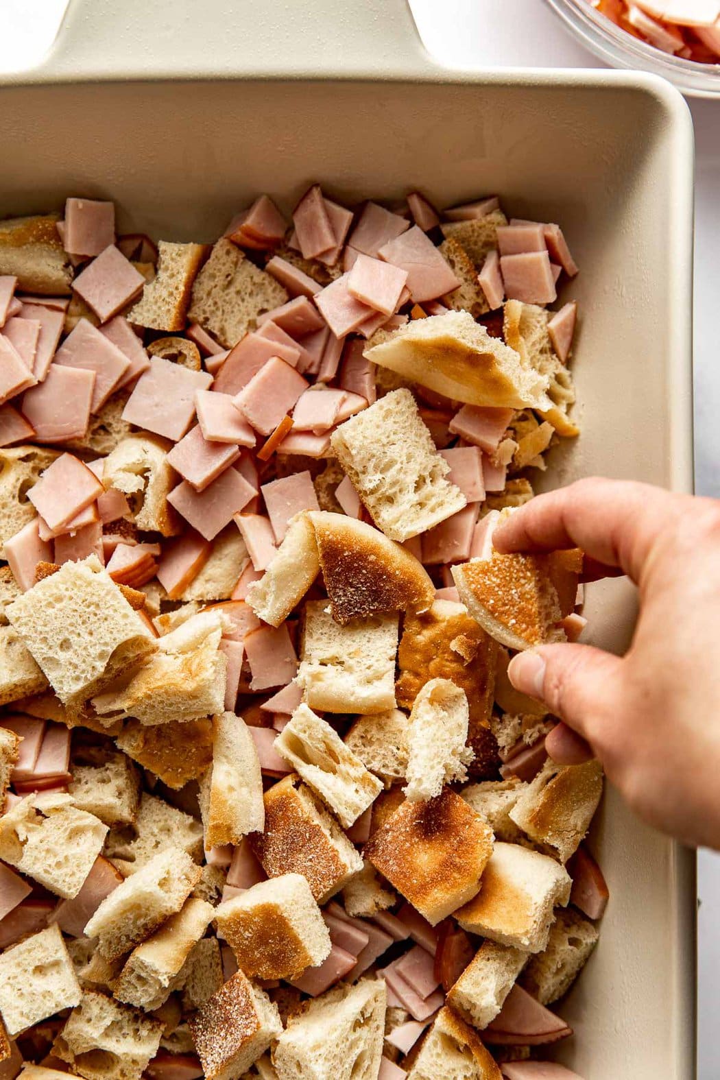 Overhead view of a hand placing english muffin pieces into a pan for Eggs Benedict Casserole. 