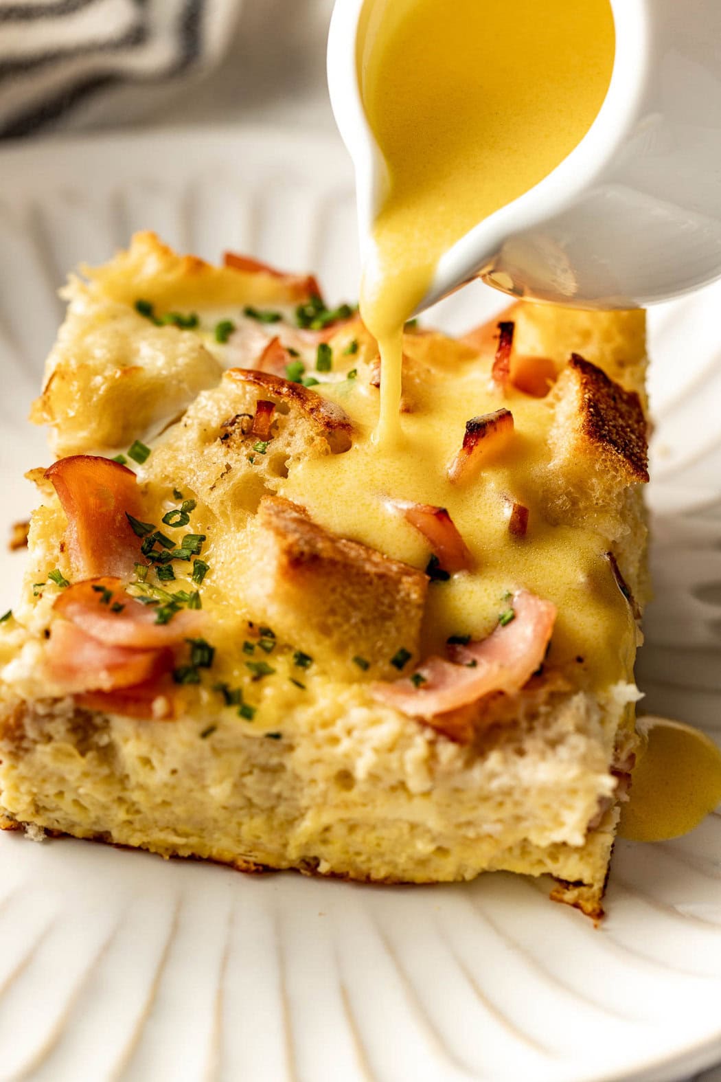 Close up view of a piece of Eggs Benedict Casserole being topped with hollandaise sauce. 