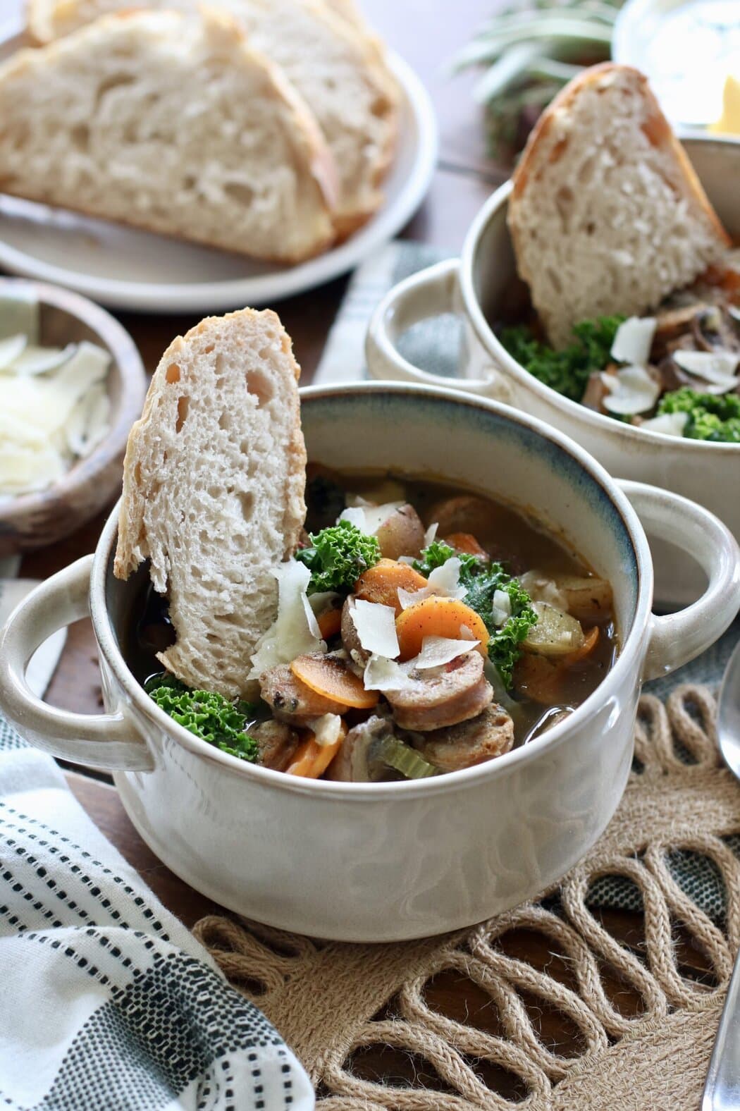 Close up view of a bowl of soup with a piece of sourdough stuck into the broth. 