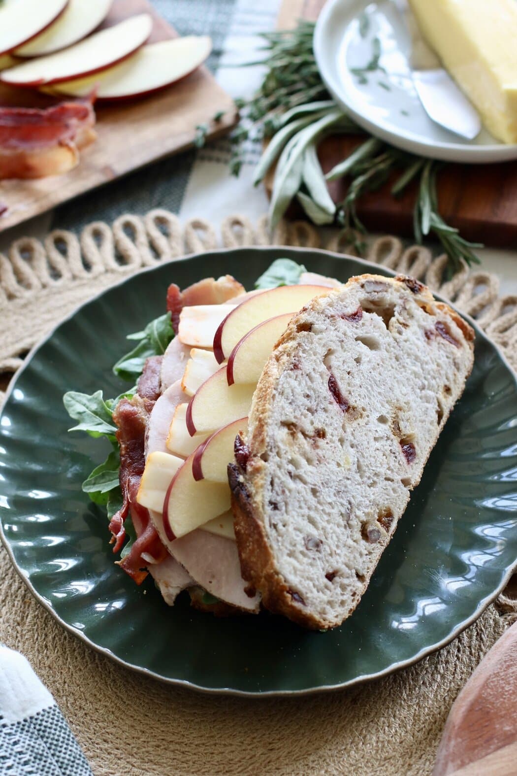 Overhead view of a plate with a fall sandwich on it showing the layers of sliced turkey, apple, and bacon. 