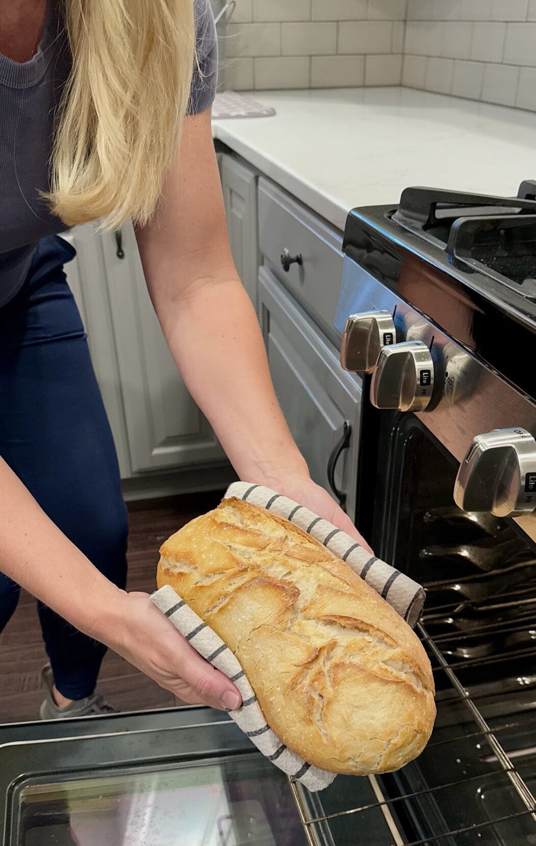 Close up view of a woman taking a loaf of sourdough out of an oven. 