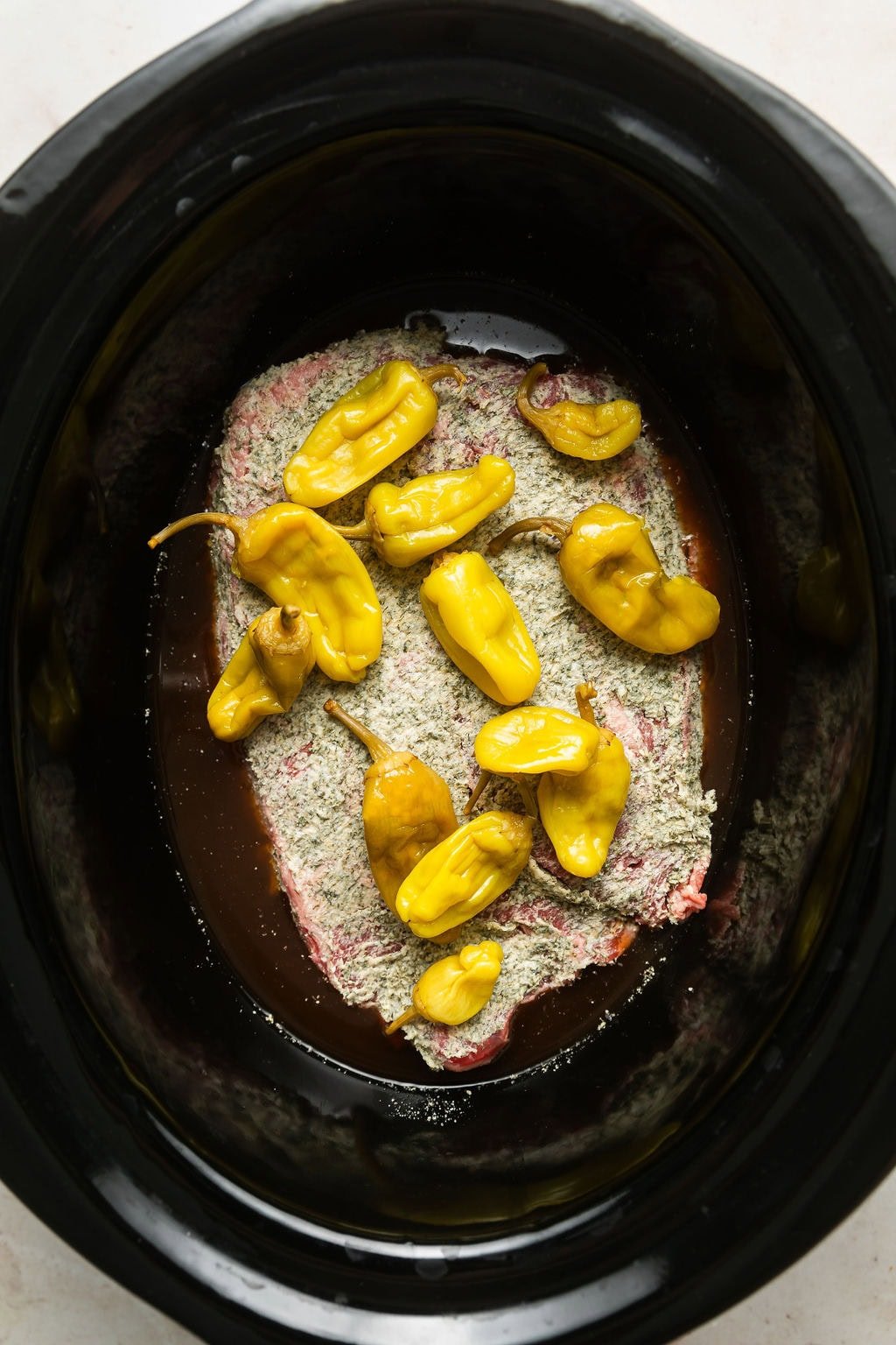 Overhead view of a slow cooker filled with Slow Cooker Mississippi Pot Roast ingredients ready for cooking.