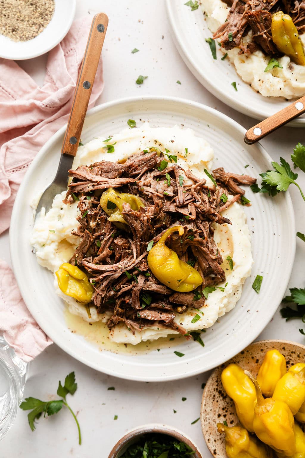 Overhead view of a plate of Slow Cooker Mississippi Pot Roast topped with black pepper and fresh herbs.