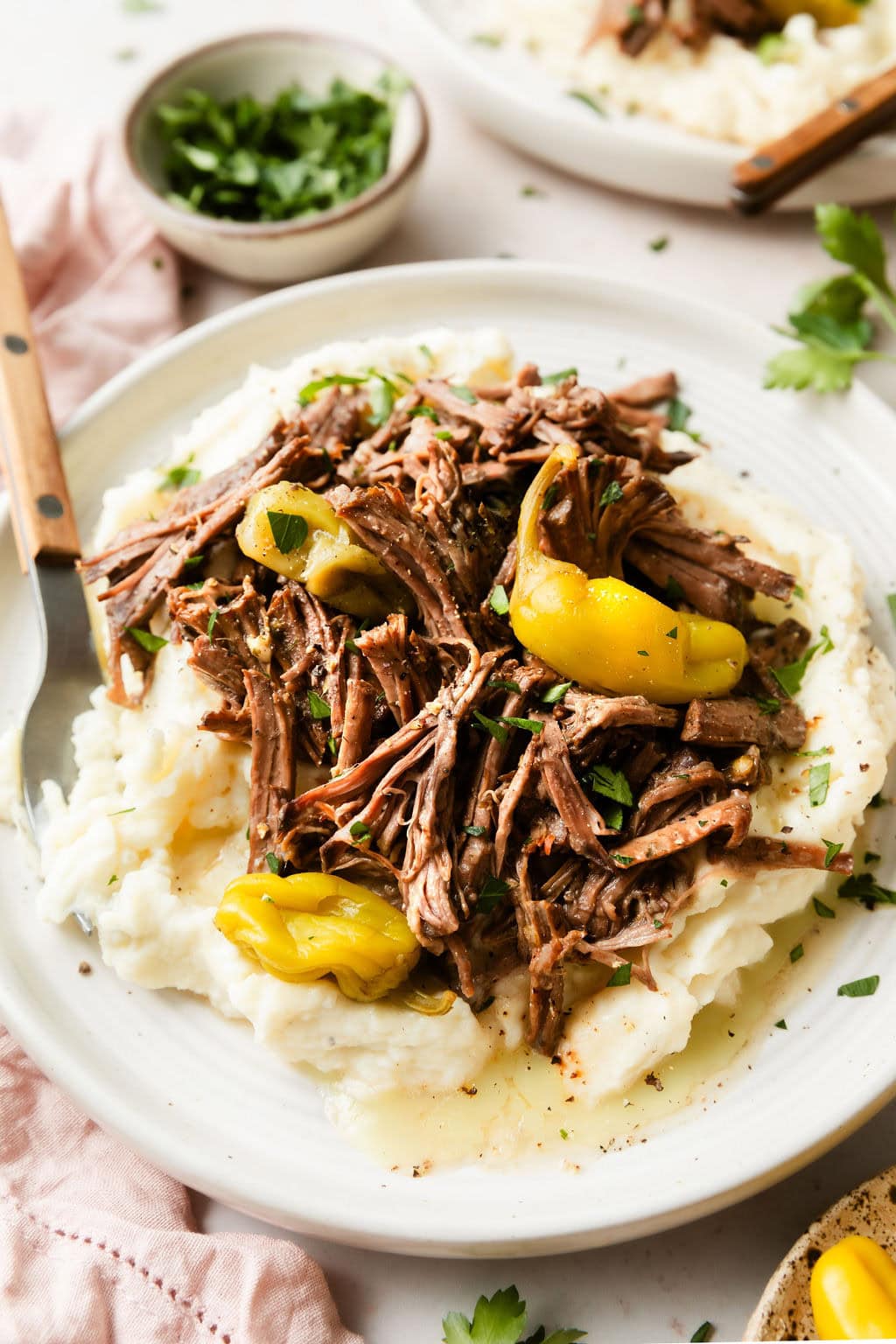 Close up view of a plate of Slow Cooker Mississippi Pot Roast topped with black pepper and fresh herbs. 