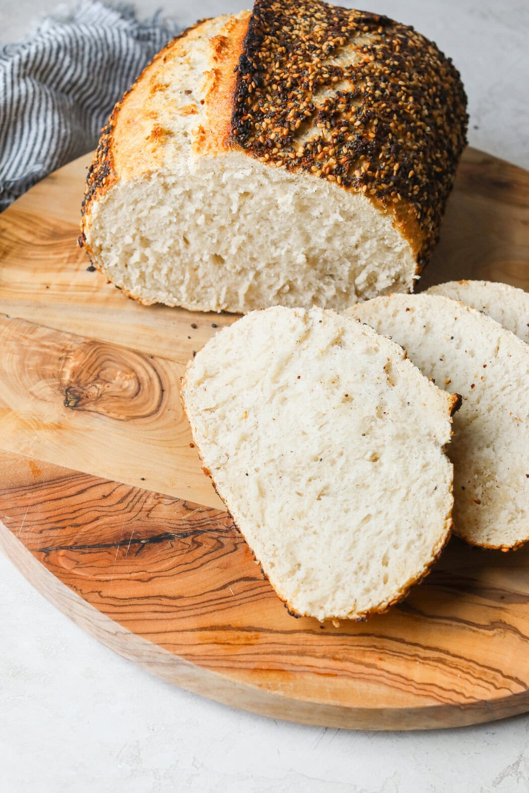 Close up view of a wooden cutting board with a freshly baked loaf of gluten-free seeded sourdough bread with it sliced to show the texture. 