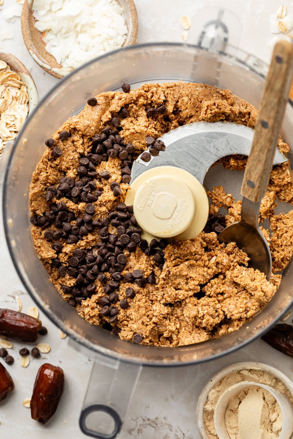 Overhead view of Almond Butter Protein Balls batter in a food processor with chocolate chips on top, ready for combining. 