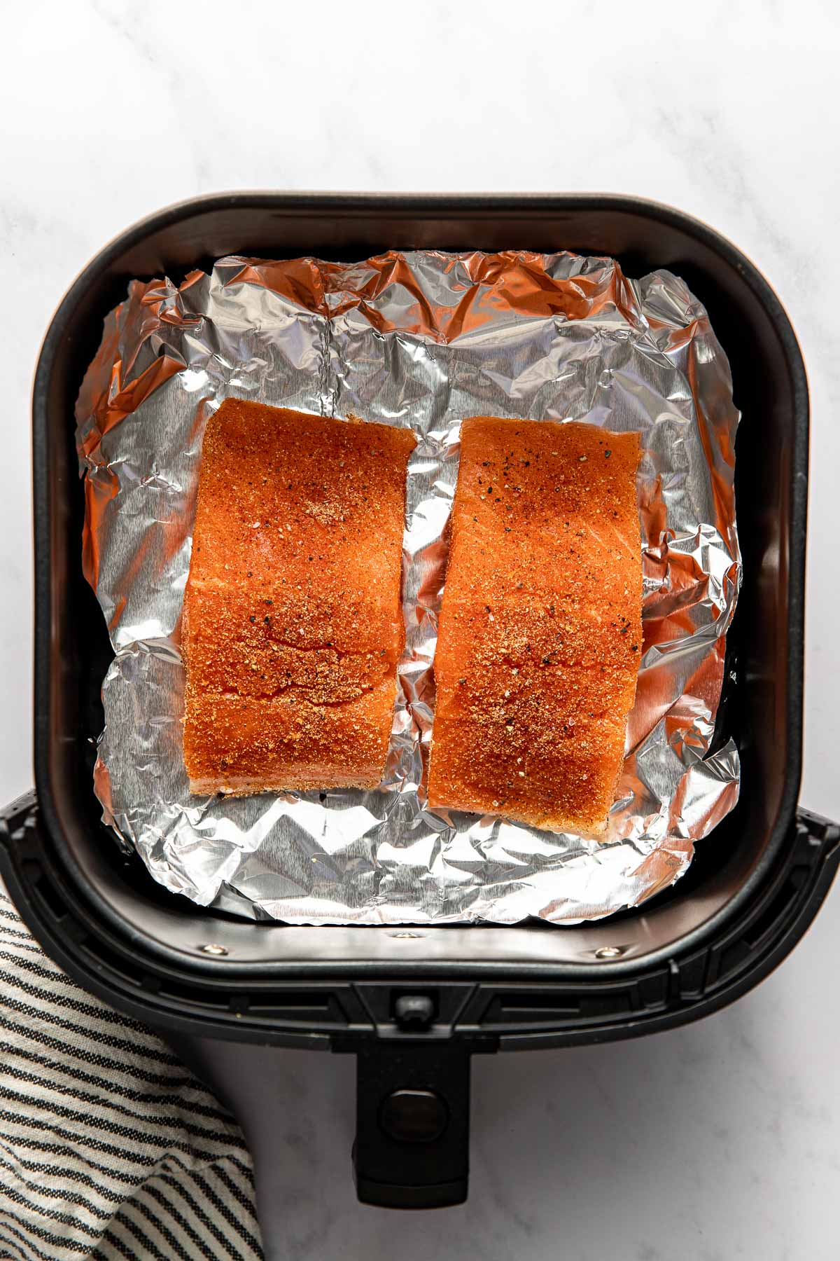 Overhead view of two salmon fillets in an air fryer basket ready for cooking. 