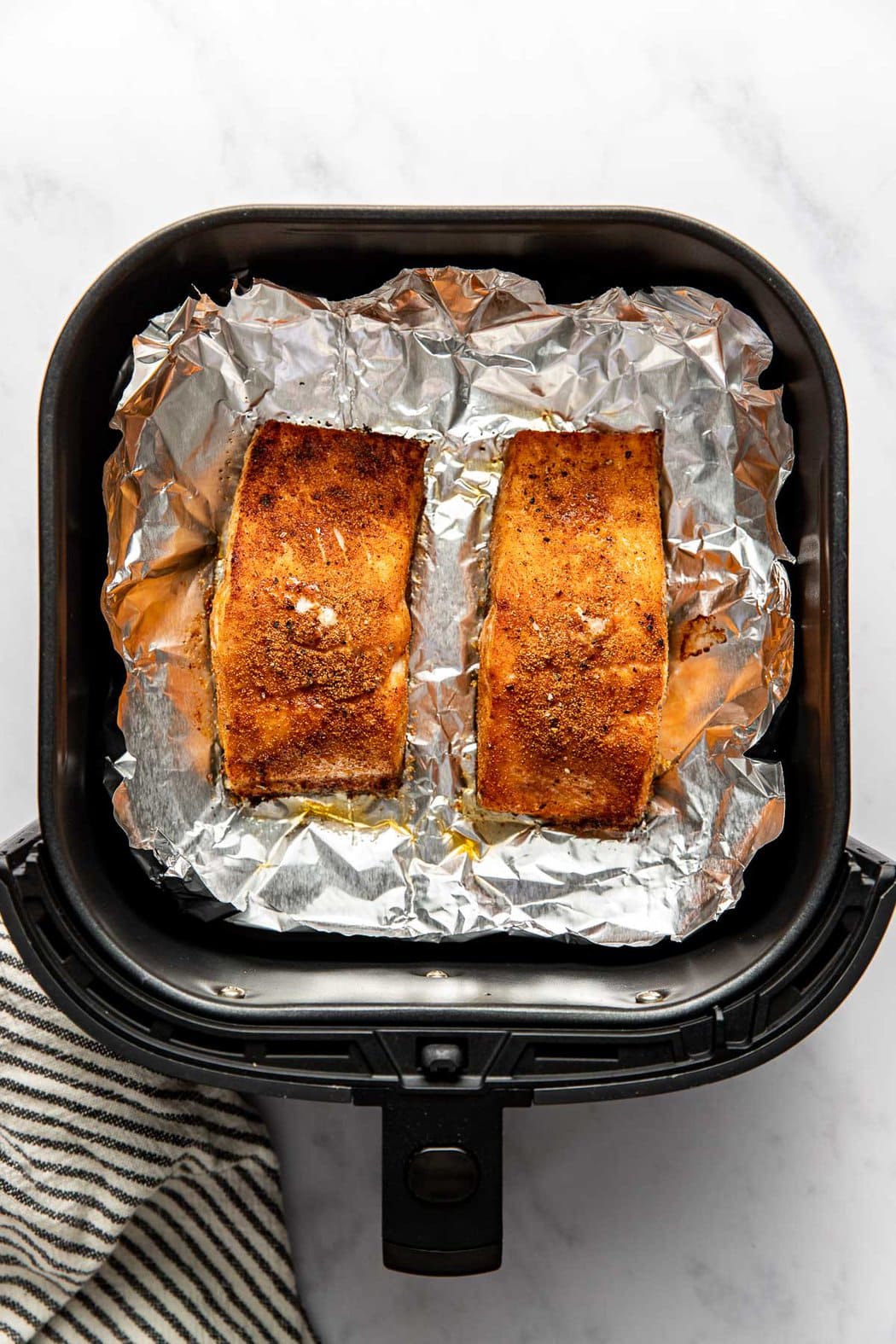 Overhead view of two cooked salmon fillets in an air fryer basket. 