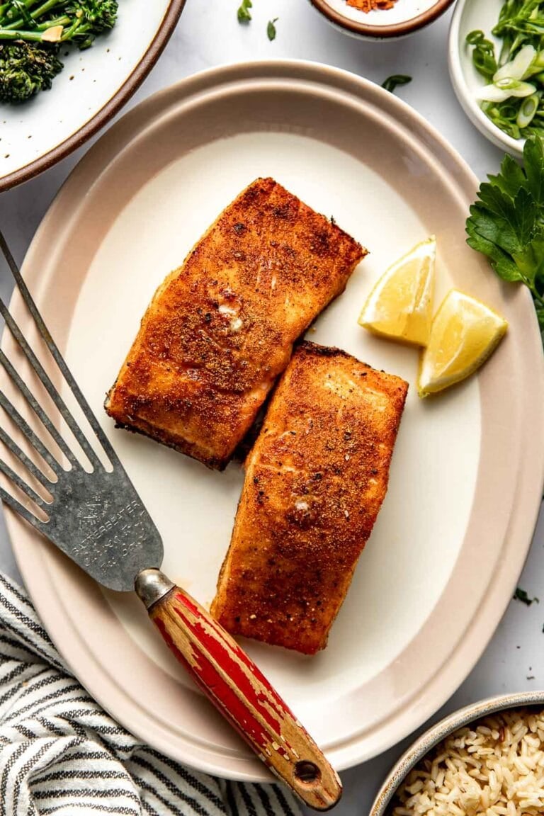 Overhead view of a plate of two crispy air fryer salmon fillets garnished with lemon wedges. 
