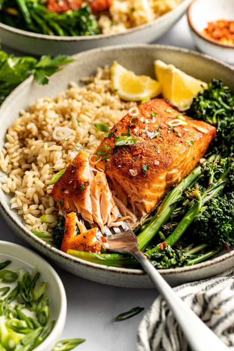 Close up view of a plate of rice and roasted vegetables alongside a piece of air fryer Salmon seasoned and topped with fresh herbs. 