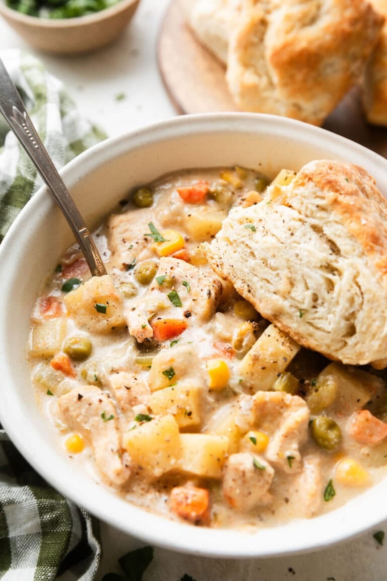 Close up view of a bowl of slow cooker chicken pot pie soup with a flakey biscuit on the side. 