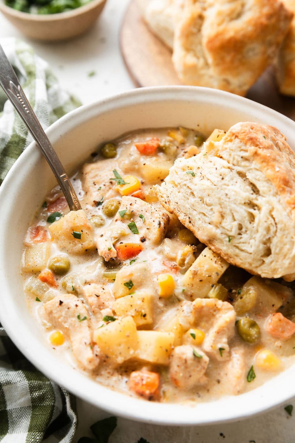 Close up view of a bowl of Slow Cooker Chicken Pot Pie Soup with a biscuit on the side. 