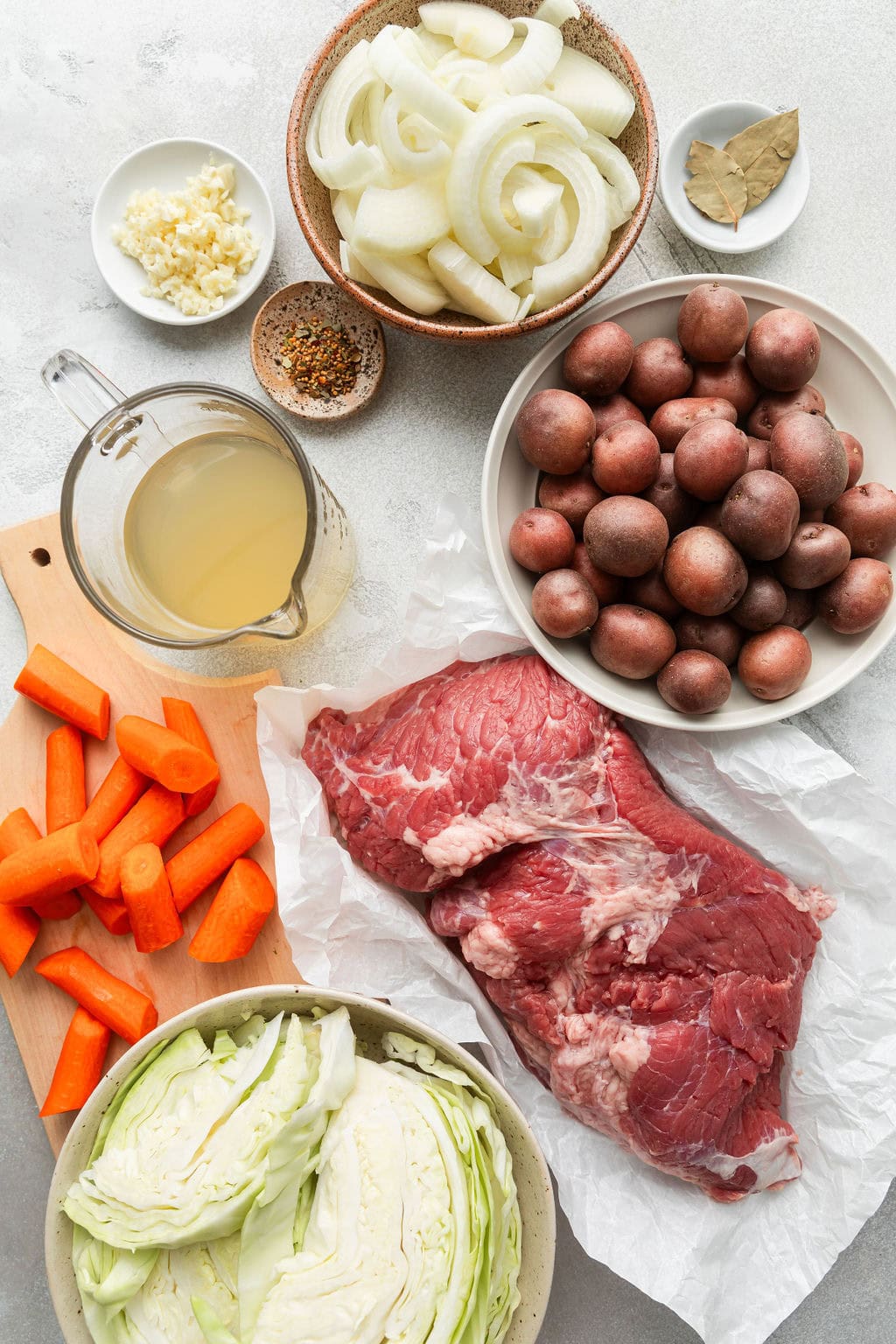 Overhead view of a variety of ingredients for Crockpot Corned Beef and Cabbage in different sized bowls. 