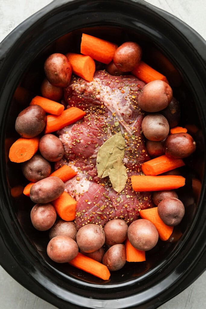 Overhead view of a slow cooker filled with ingredients for Crockpot Corned Beef and Cabbage. 