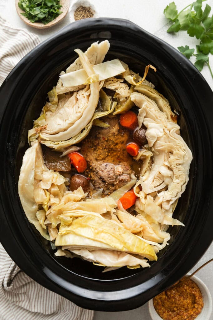 Overhead view of a slow cooker filled with ingredients for Crockpot Corned Beef and Cabbage. 