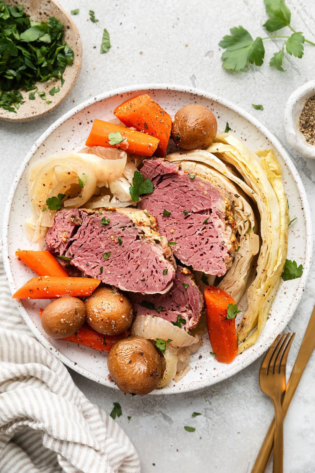 Overhead view of a plate of Crockpot Corned Beef and Cabbage topped with fresh herbs and black pepper. 