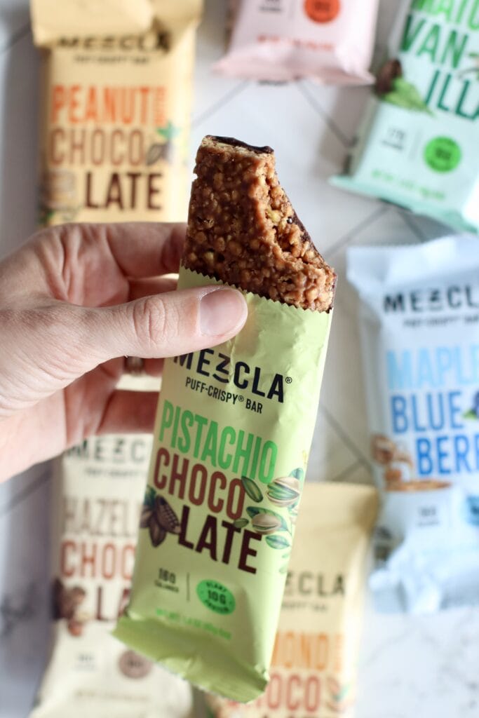 Close up view of a hand holding an opened mezcla bar with a bite out of the top to show the texture of the bar.