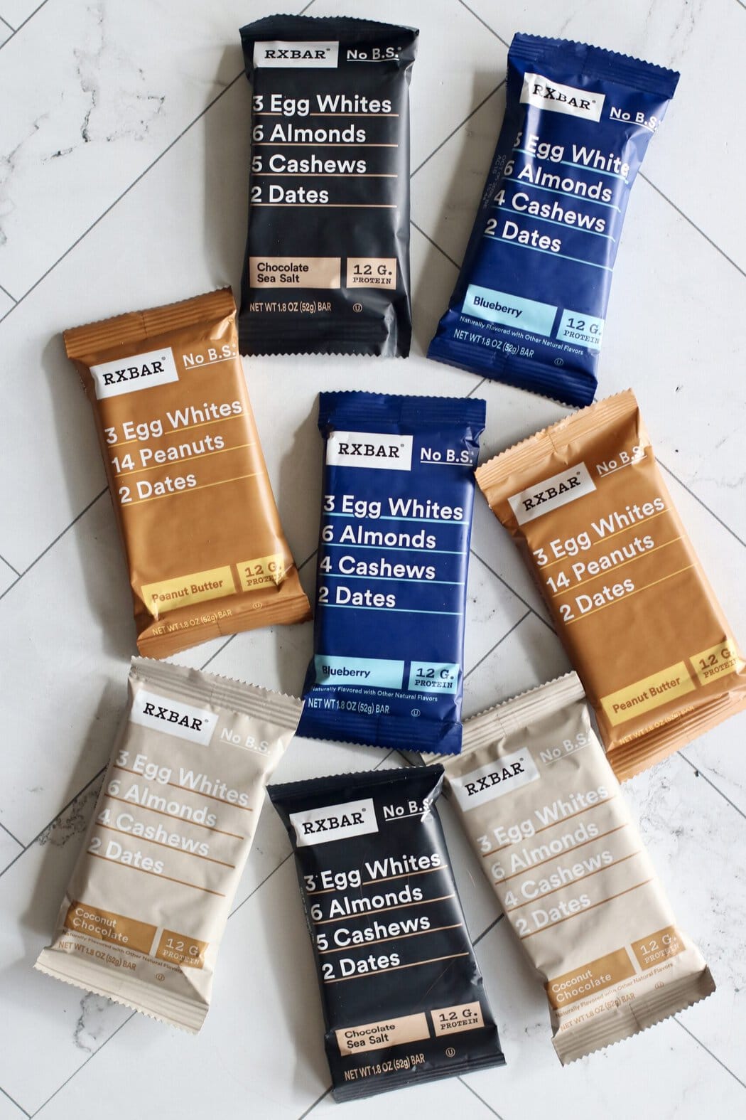 Overhead view of a variety of RX protein bars arranged on a white marble countertop.