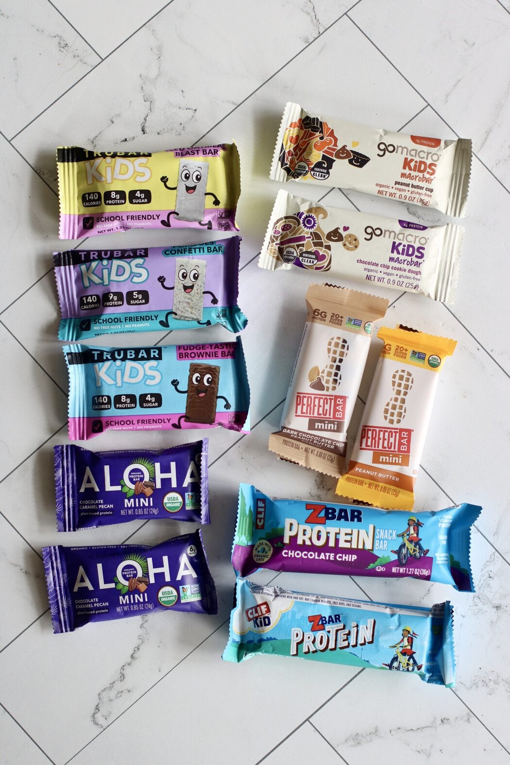 Overhead view of a variety of kids protein bars arranged on a white marble countertop.