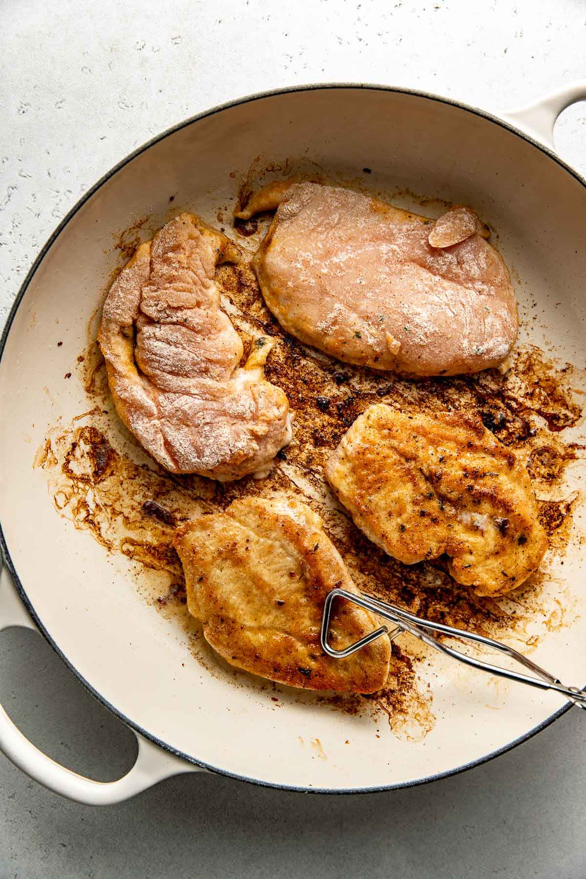 Overhead view of four chicken breasts being fried in a skillet. 