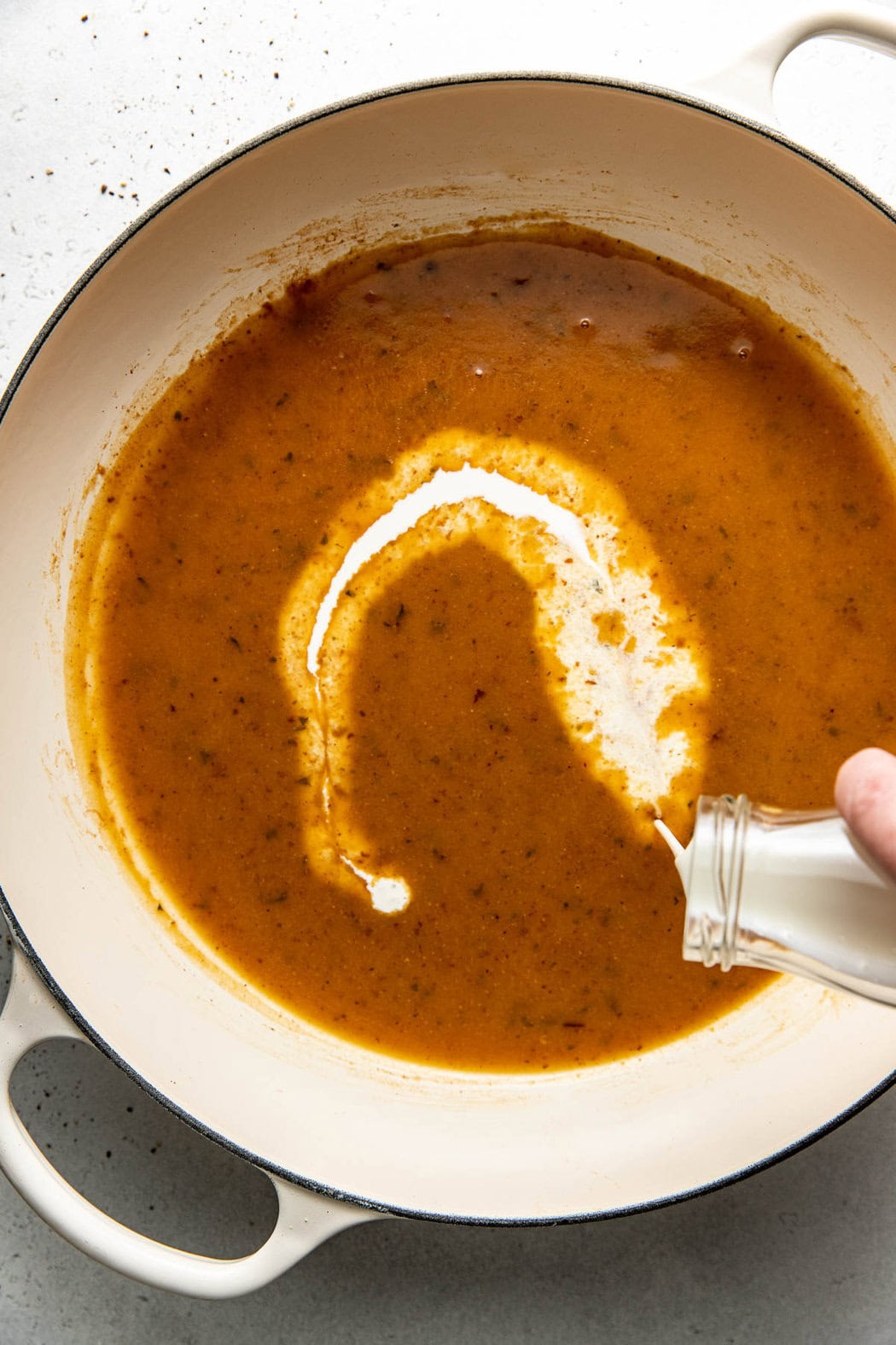 Overhead view of a gravy mixture in a skillet with cream being poured in. 