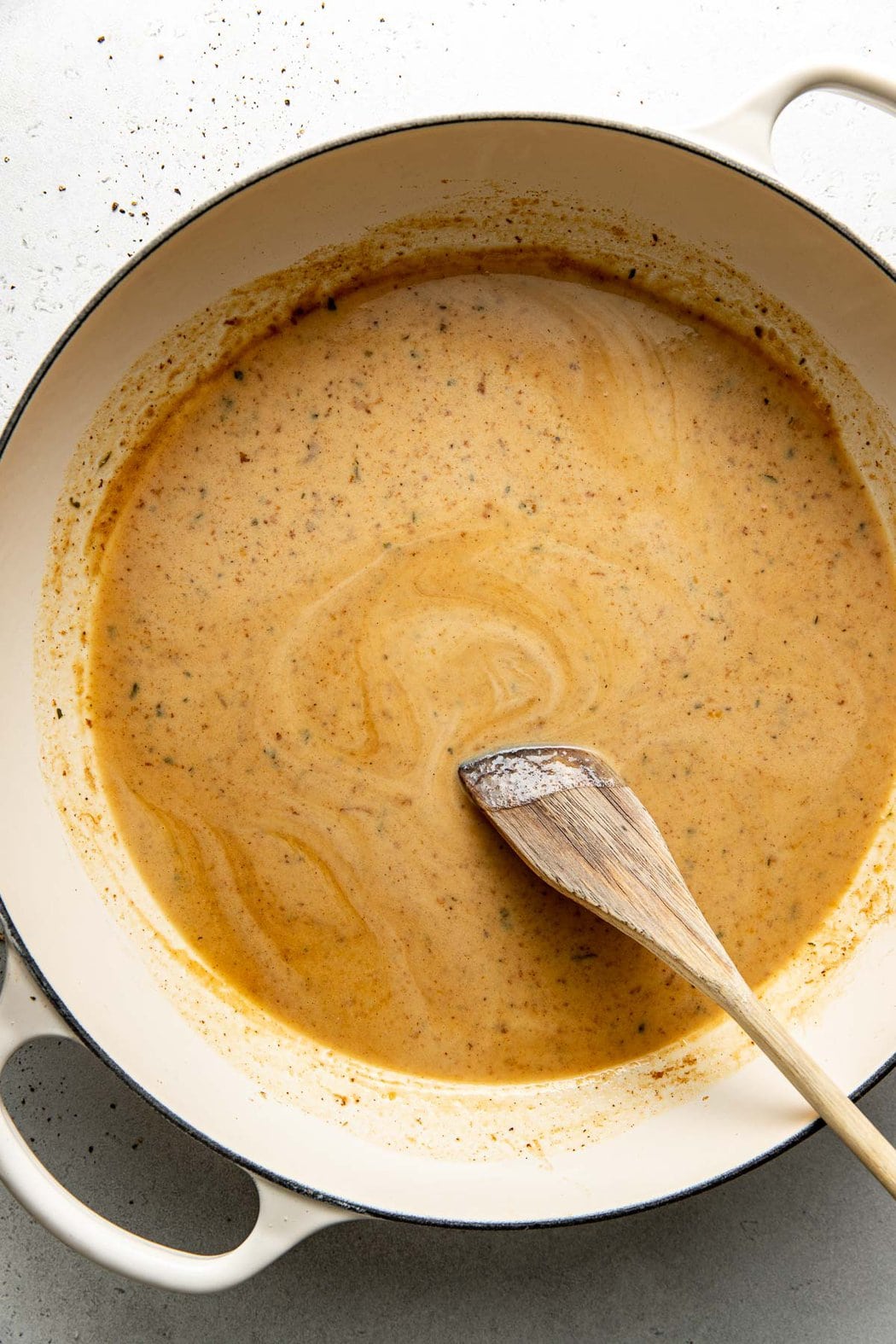 Overhead view of a wooden spoon stirring a gravy mixture in a skillet. 