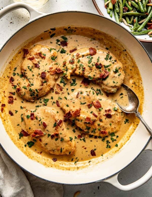 Overhead view skillet filled with smothered chicken recipe topped with crisp pieces of bacon