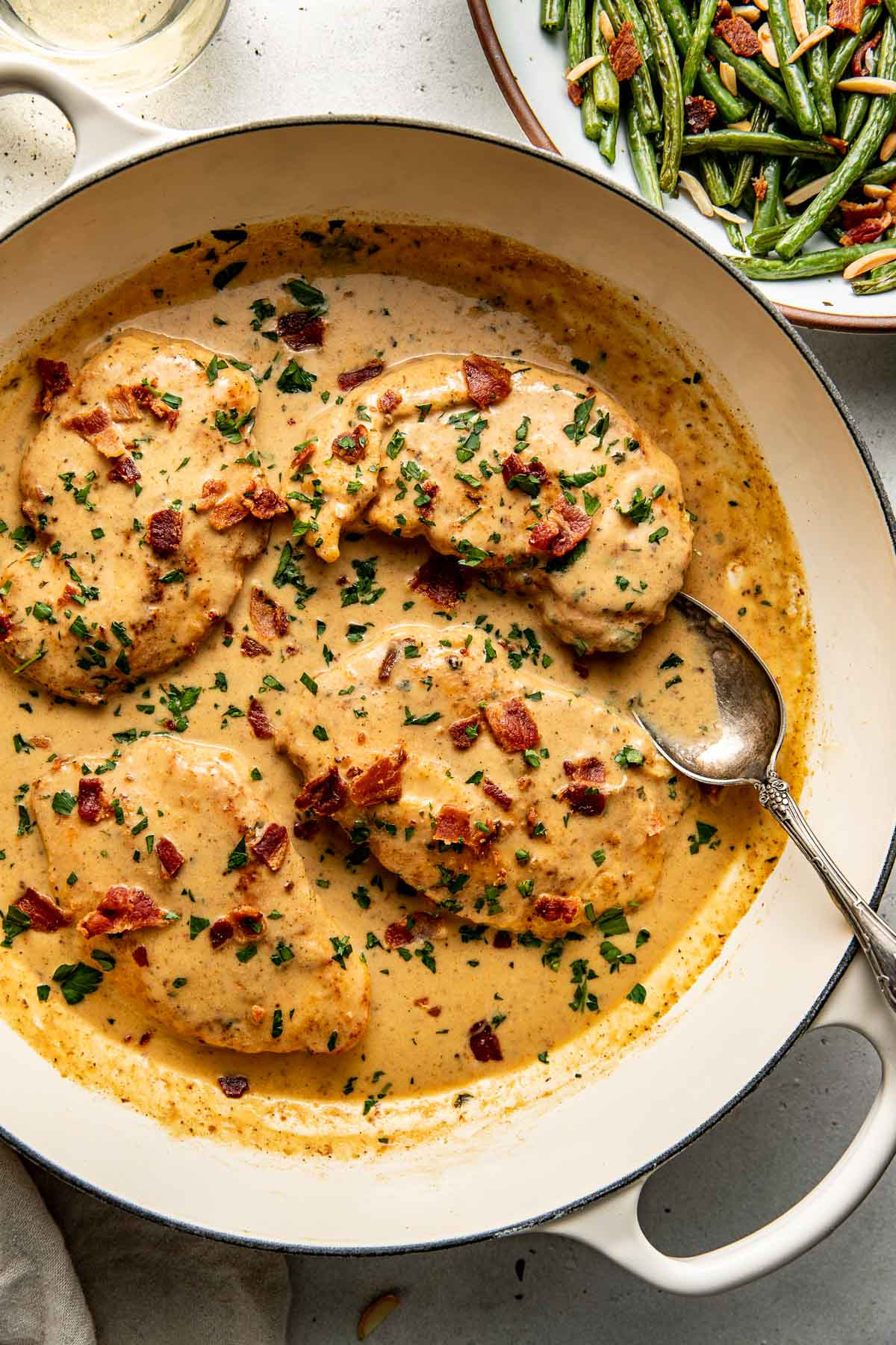 Overhead view of a skillet of Smothered Chicken topped with fresh herbs and bacon pieces. 