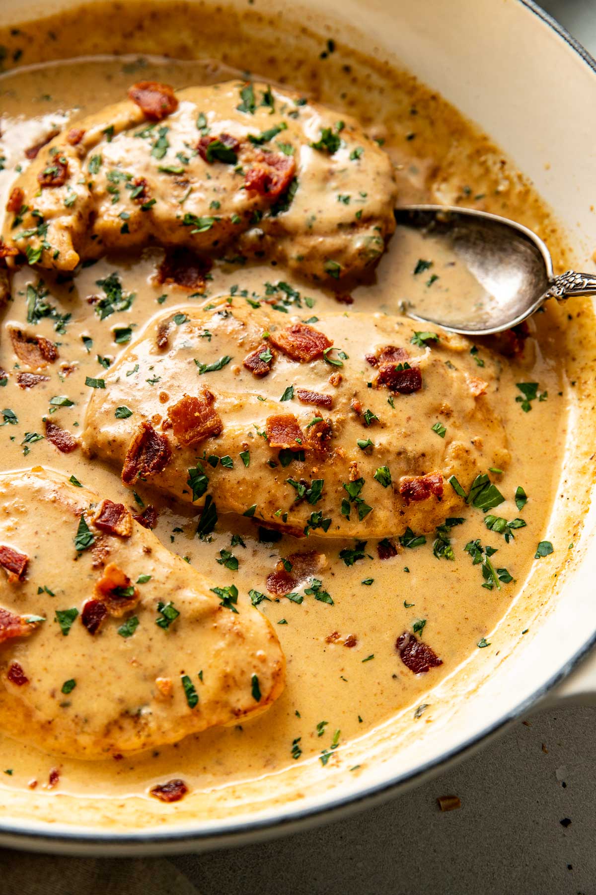 Overhead view of Smothered Chicken in a skillet with a spoon scooping some of the gravy mixture between the chicken breasts. 