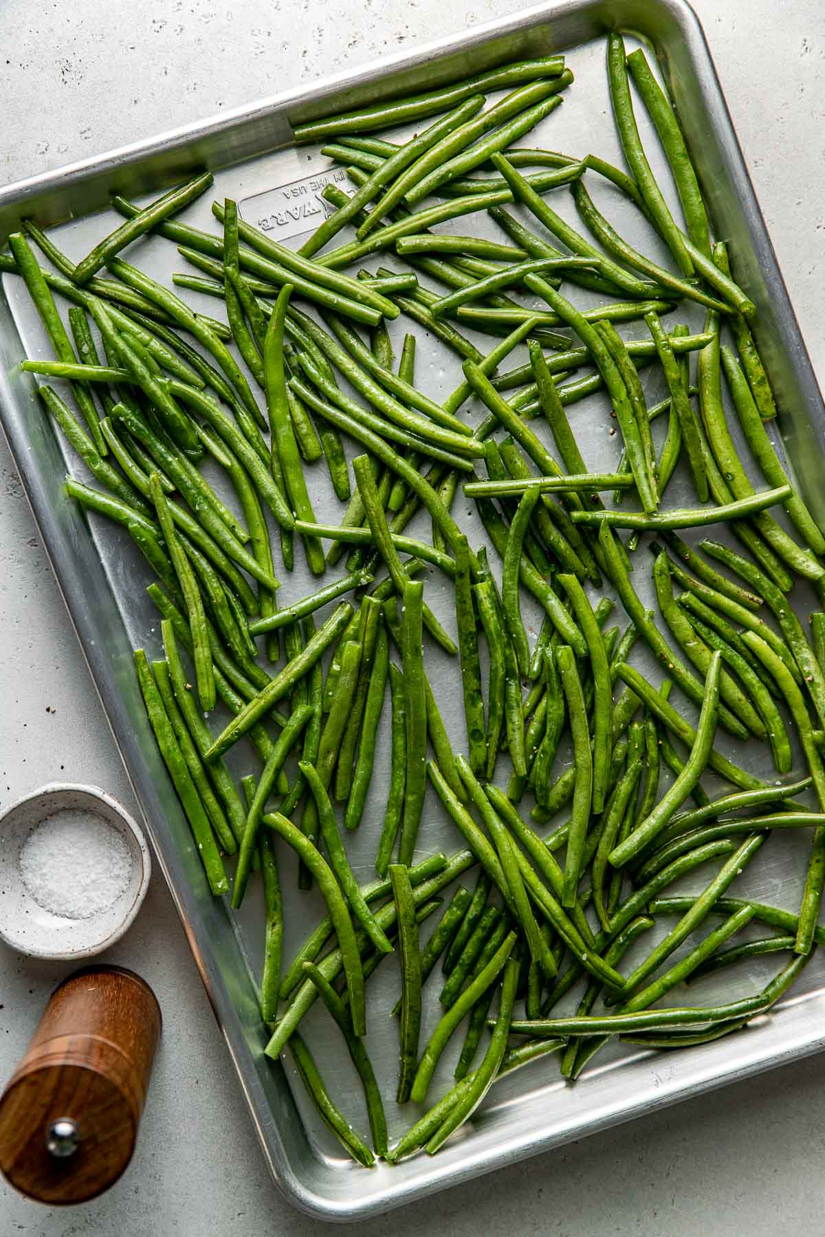 Overhead view of a sheet pan filled with fresh green beans topped with olive oil and salt. 