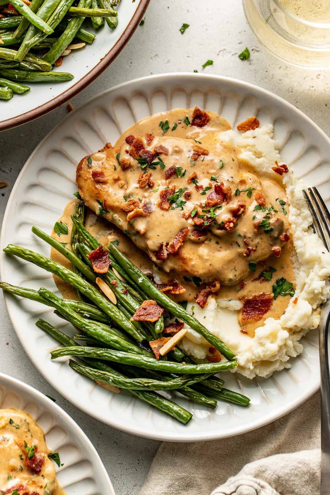 Overhead view of a plate of Smothered Chicken next to mashed potatoes and roasted green beans. 