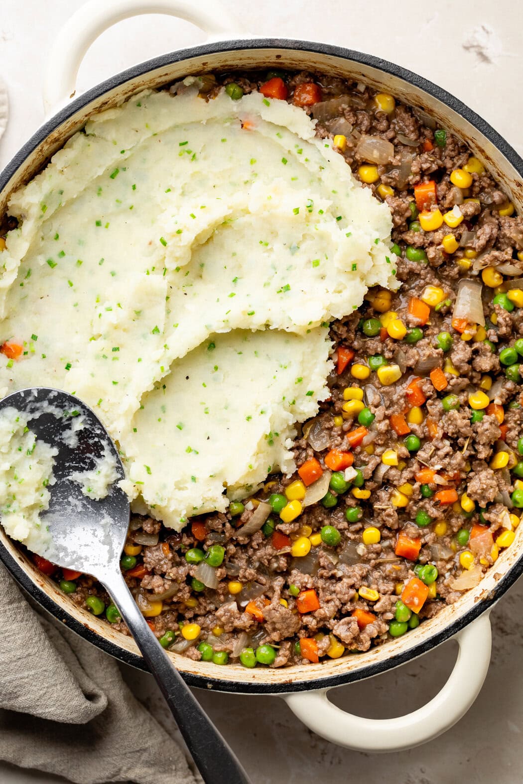 Overhead view of a skillet of Cottage Pie With Garlic Mashed Potatoes being spread on top. 