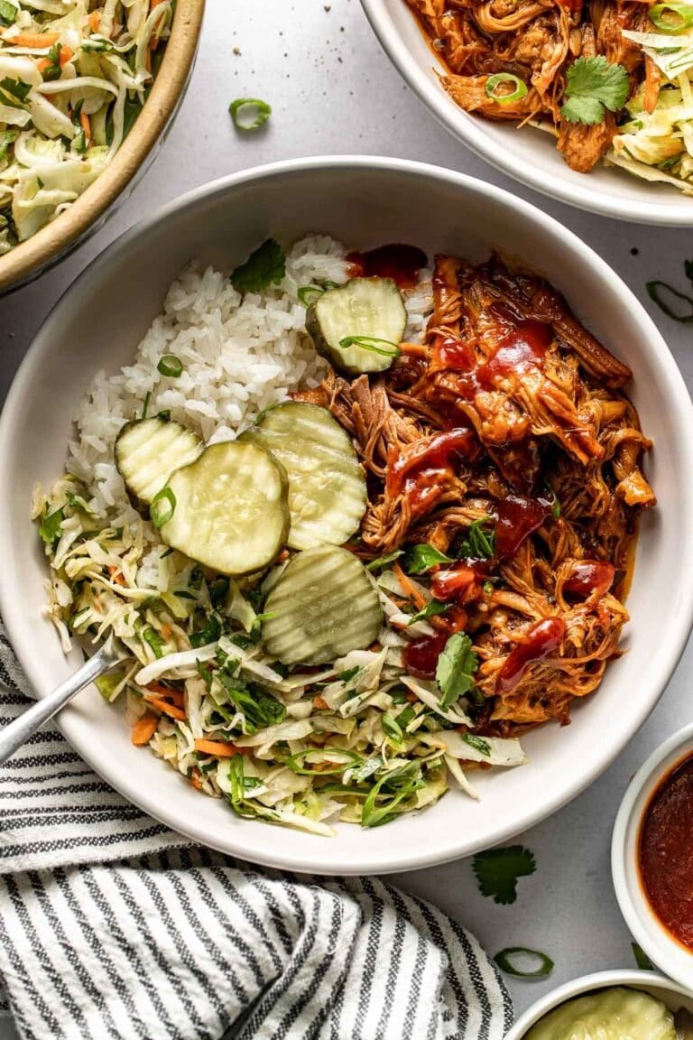 A crockpot pulled pork bowl topped with BBQ sauce and sliced pickles. 