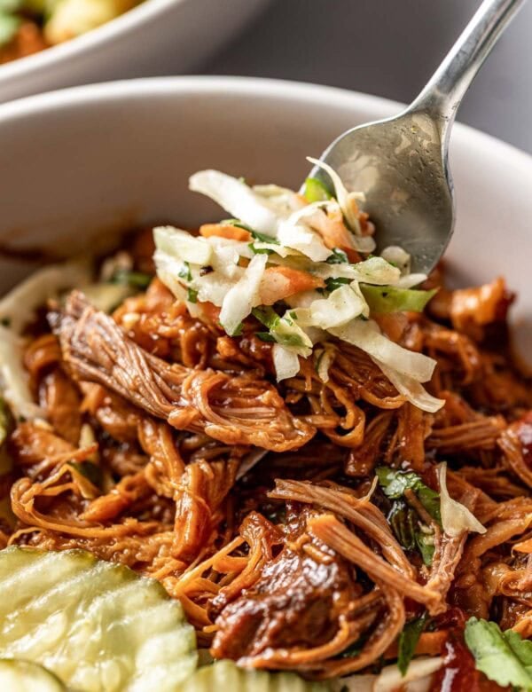 A forkful of coleslaw and pulled pork being taken from a bowl