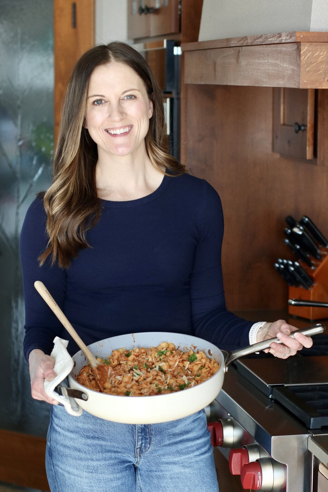 Woman holding a skillet filled with a tomato pasta topped with fresh cheese and herbs. 